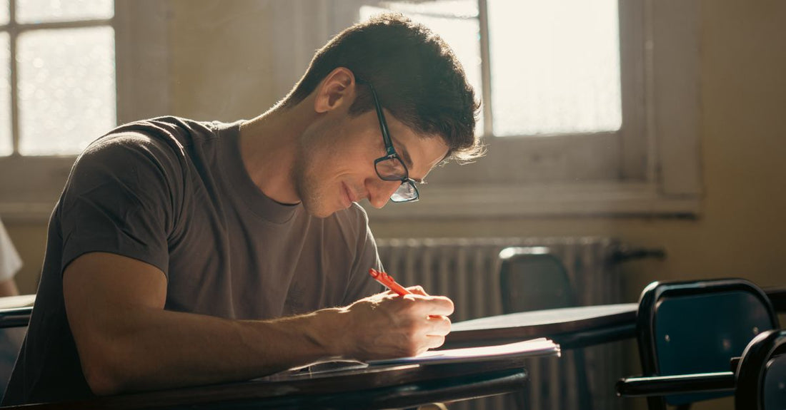 Focused student writing in a sunlit classroom during finals week